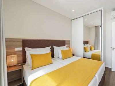 Modernes Schlafzimmer mit Doppelbett, gelben Kissen und Decke, Spiegelschrank und Nachtlampe.