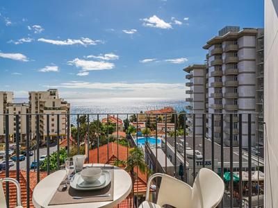 Balkon mit Essplatz, Blick auf Stadt, Meer, Pool und bewölkten Himmel am Tag.