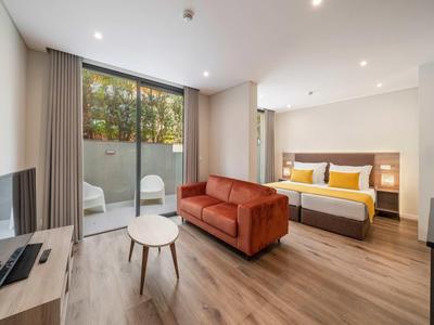 Moderner Hotelzimmer mit Doppelbett, rotem Sofa, Holzboden und Glas-Schiebetür zum Balkon.
