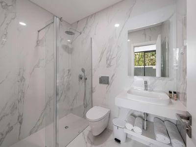 Modernes weißes Badezimmer mit Glasdusche, Waschbecken, Toilette und großer Spiegelwand.