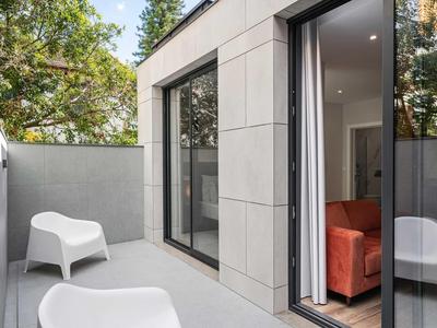Moderner Balkon mit grauen Fliesen, weißen Stühlen und Blick auf grüne Bäume im Hintergrund.