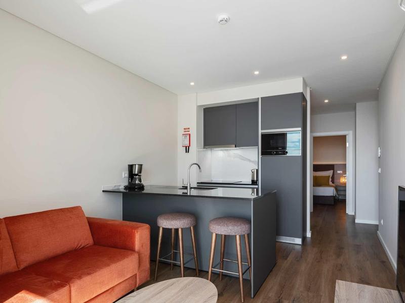 Moderner Wohnraum mit braunem Sofa, schwarzer Kücheninsel, Holzstuhl und offenem Flur.