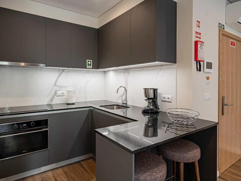 Moderne kleine Küche mit grauen Schränken, Marmor-Arbeitsfläche und zwei Barhockern.