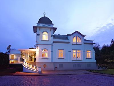 Großes, weißes Haus mit Turm, vielen Fenstern und beleuchtet in der Dämmerung.