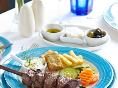 Un piatto con carne alla griglia, patatine, verdure e salse su un tavolo bianco con vino e acqua.