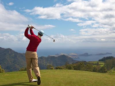 Un golfista con maglione rosso colpisce su un campo da golf verde con vista sul mare.