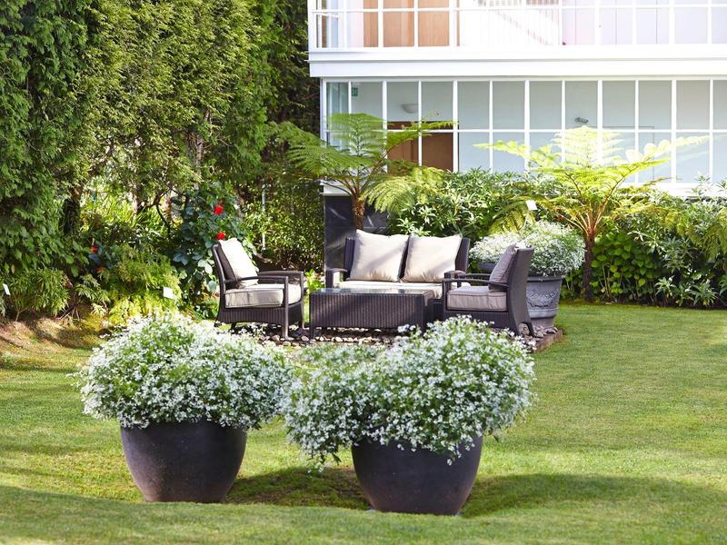 Set di sedute da giardino moderno su prato curato con rigogliosa vegetazione sullo sfondo