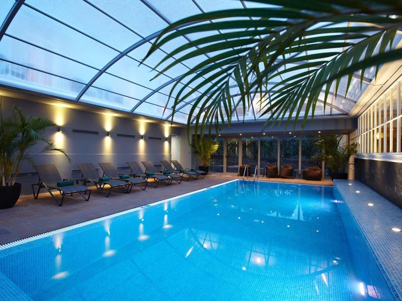 Piscina coperta riscaldata con tetto in vetro e piante in un ambiente alberghiero rilassante.