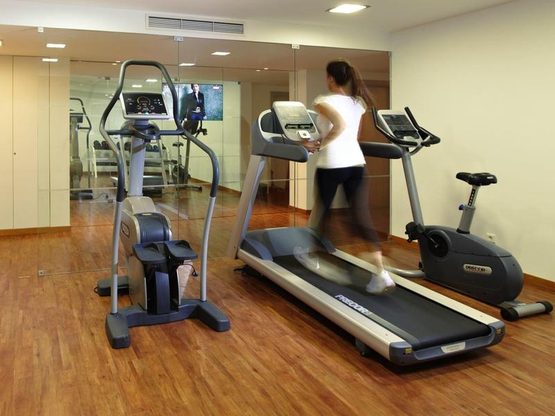 Donna che corre su un tapis roulant in una palestra con bici e ellittica.