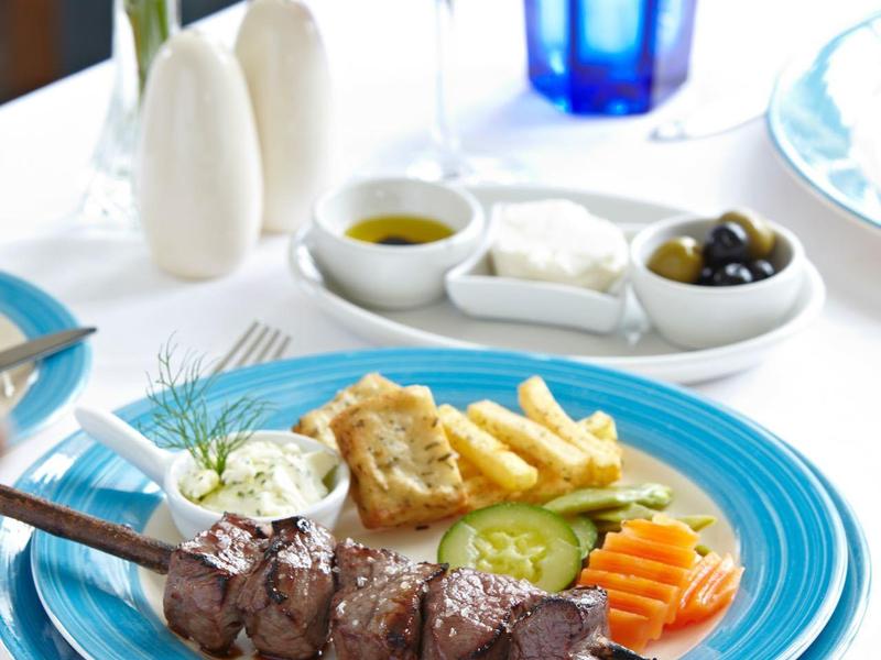 Un piatto con carne alla griglia, patatine, verdure e salse su un tavolo bianco con vino e acqua.