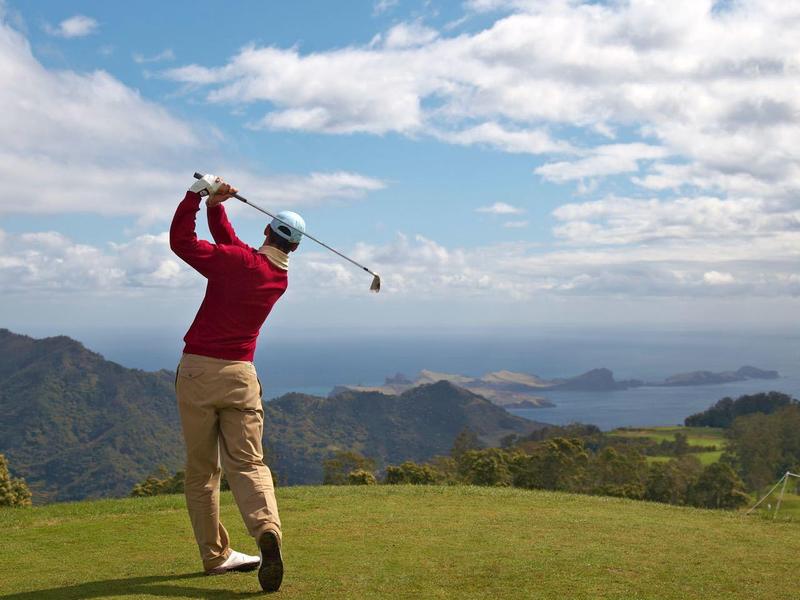 Un golfista con maglione rosso colpisce su un campo da golf verde con vista sul mare.