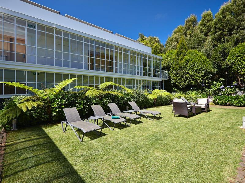 Giardino moderno dell'hotel con lettini e sedute su prato curato davanti a una facciata in vetro.