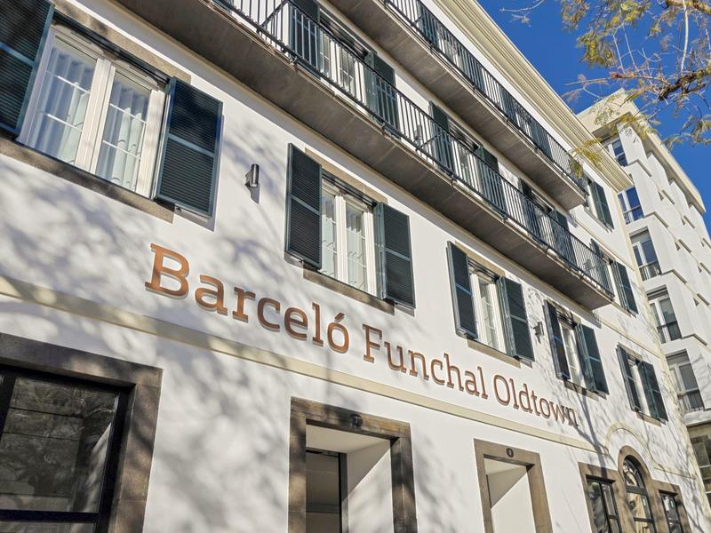 Uitzicht op de buitenkant van hotel Barceló Funchal Coliseum met duidelijke bewegwijzering onder een blauwe lucht.