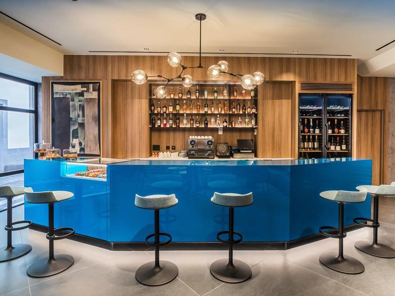 Moderne hotelbar met blauwe bar, houten planken en vijf barkrukken.