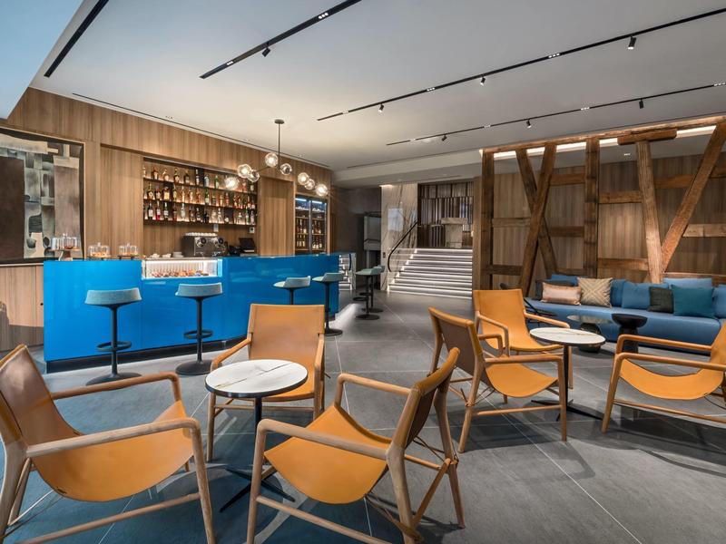 Moderne hotellounge met houten wandbekleding, blauwe bar en comfortabele leren stoelen.