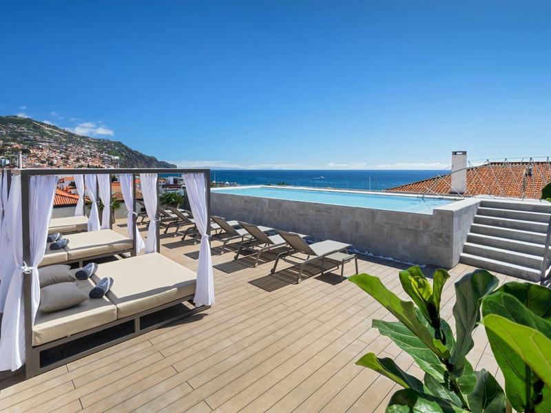 Terras met ligstoelen, hemelbedden en uitzicht op zee onder een heldere hemel.