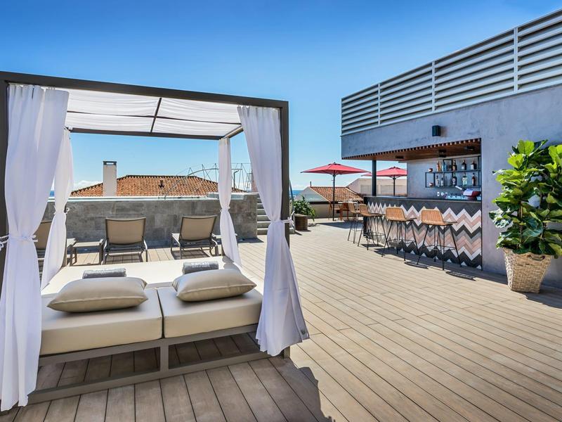 Moderne hotelterras met dagbed, bar en zeezicht bij helder weer.