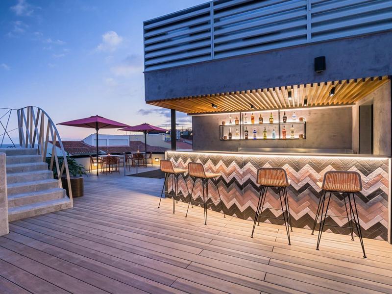 Moderne hotelbar met houten terras en krukken bij zonsondergang buiten.
