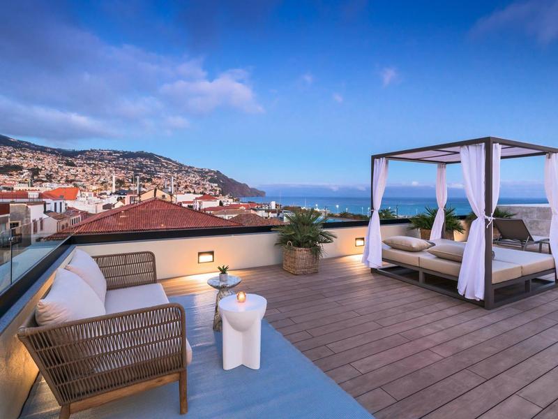 Dakterras met lounge meubels, hemelbed en uitzicht op stad en zee bij zonnige hemel.