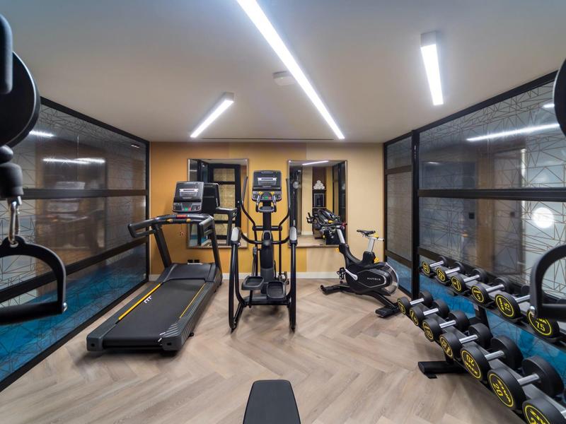 Moderne fitnessruimte met loopband, roeimachine en halters in een hotel.