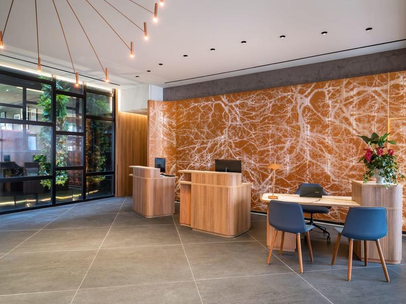 Moderne hotellobby met houten balie, decoratieve muur en zithoek met blauwe stoelen.