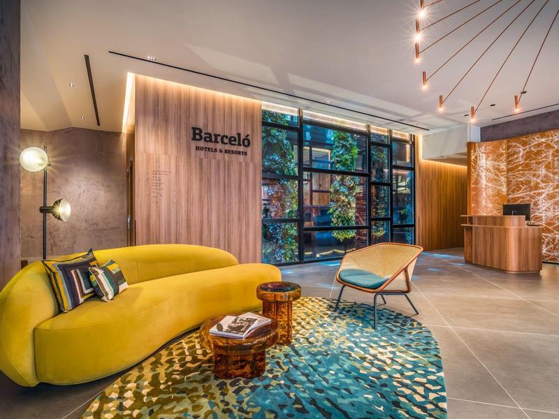 Moderne hotel lobby met gele bank, stoelen en kleurrijk vloerkleed in warm licht.