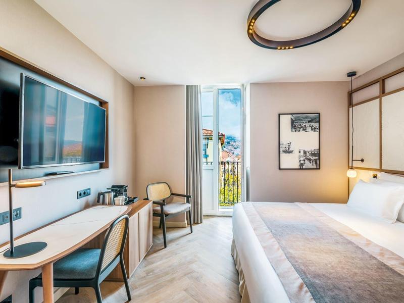 Moderne hotelkamer met tweepersoonsbed, bureau, tv en balkon met bergzicht.