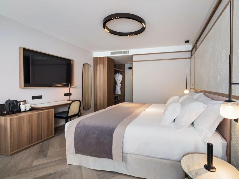 Moderne hotelkamer met groot bed, bureau, tv en open badkamerdeur.