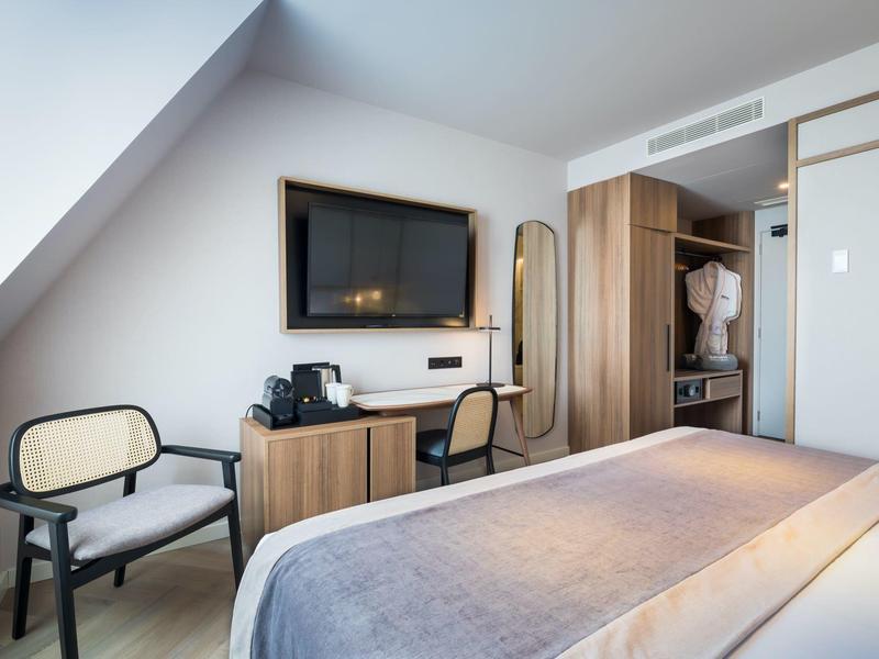 Modern hotelkamer met tv, twee stoelen en eenvoudige inrichting onder een schuin plafondraam.