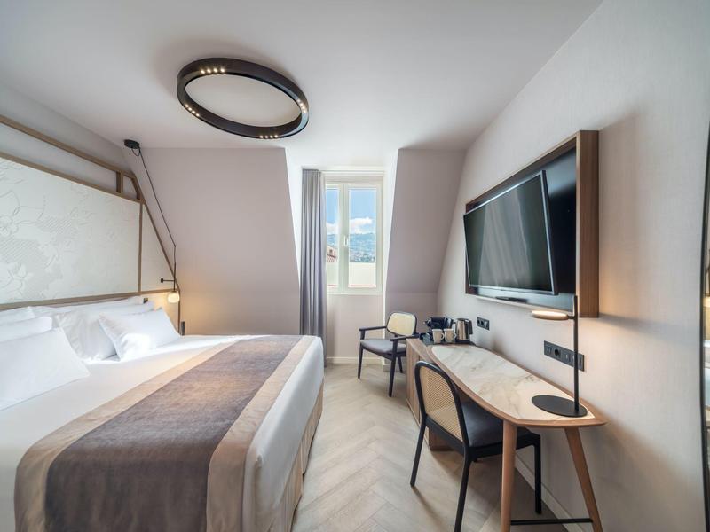 Moderne hotelkamer met groot bed, bureau, stoelen en groot raam met uitzicht op zee.