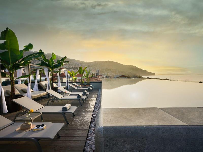 Infinitypool met ligbedden en palmbomen met uitzicht op bergen bij zonsondergang.