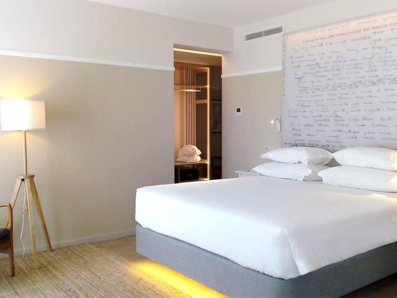 Chambre d'hôtel moderne avec grand lit, chaise, lumière chaude et décoration élégante.