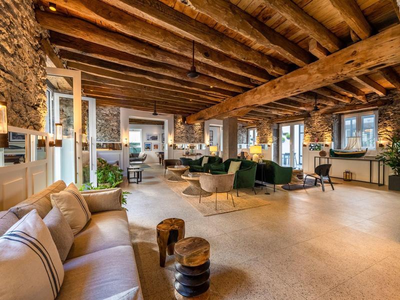 Salon d'hôtel accueillant avec poutres en bois, murs en pierre et sièges modernes.