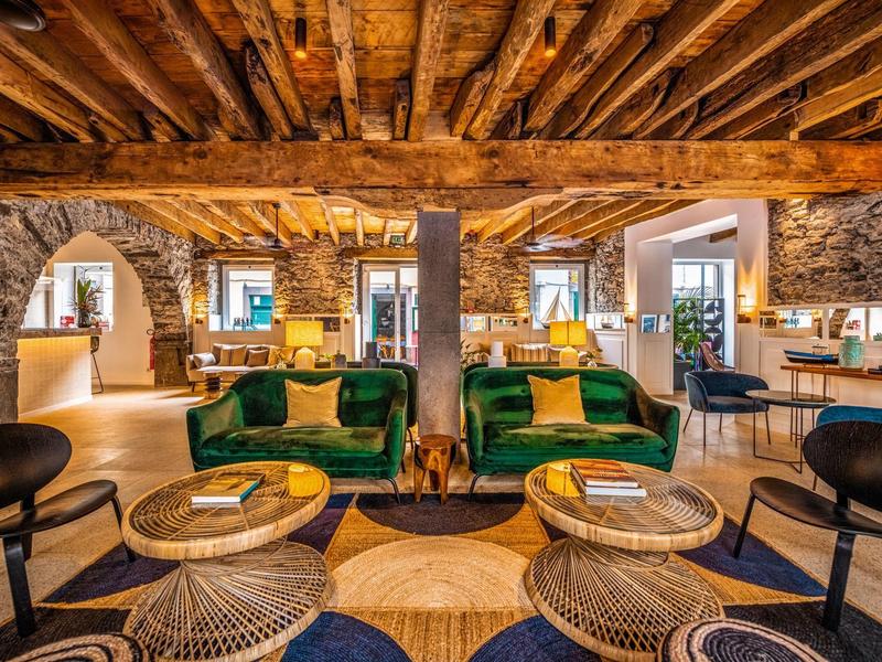Espace lounge d'hôtel accueillant avec fauteuils verts, plafond en poutres et colonnes en pierre rustiques.
