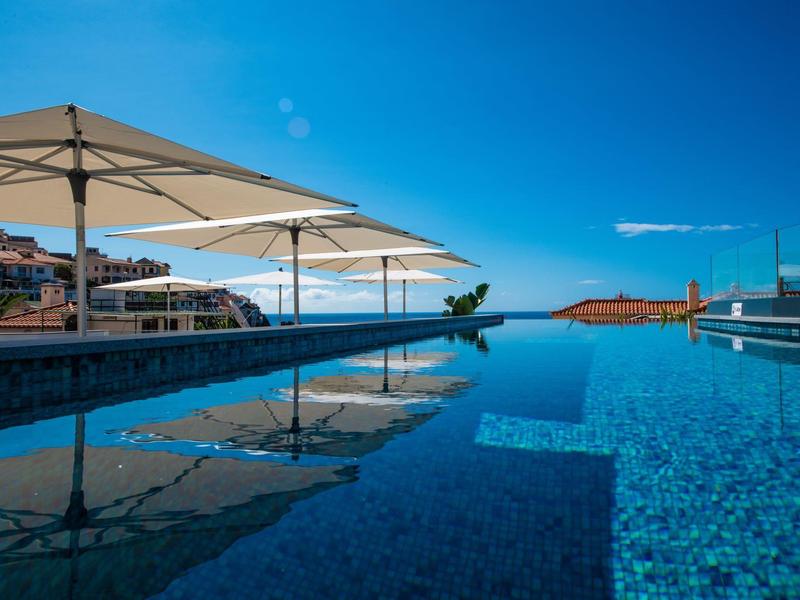 Piscine à débordement avec parasols à côté de la mer et ciel bleu clair