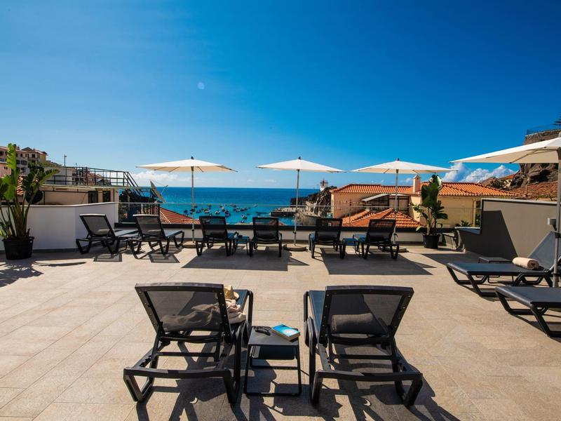 Terrasse ensoleillée avec chaises longues et coins salon avec vue sur la mer sous un ciel clair.