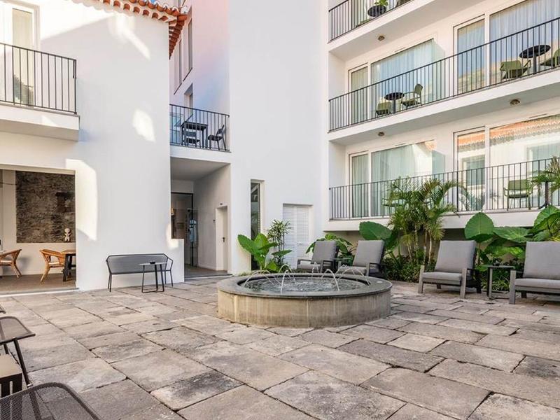 Cour intérieure d'hôtel moderne avec fontaine, chaises longues et plantes pour des moments de détente.