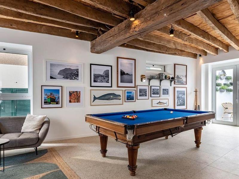 Intérieur avec table de billard, plafond avec poutres en bois, canapé et mur décoré de photos encadrées.