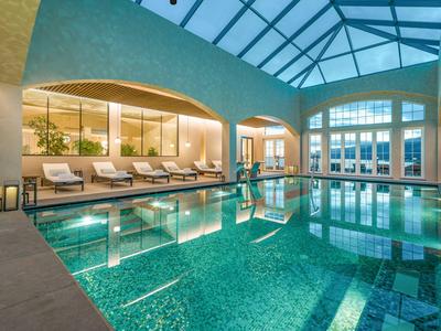 Bright indoor pool with lounge chairs and large windows in a hotel.
