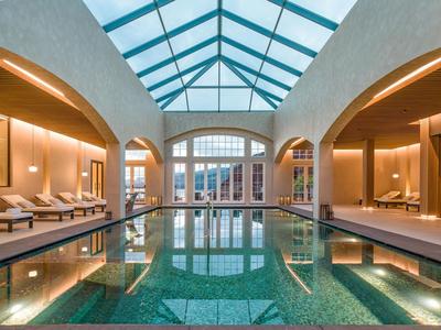 Indoor pool with glass roof and comfortable lounge chairs in a luxurious spa area.