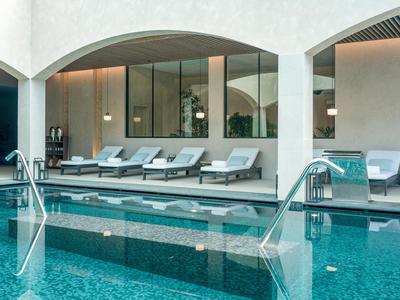 Modern indoor pool with comfortable loungers and large windows in a hotel.