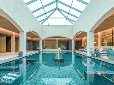 Modern indoor pool with glass roof and comfortable lounge chairs in a hotel.