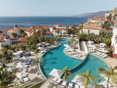 Hotelpool mit Liegestühlen und Blick auf das Meer, umgeben von mediterranen Gebäuden.