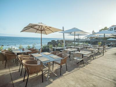 Sonnige Terrasse mit Stühlen, Tischen und Schirmen mit Blick aufs Meer.
