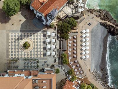 Vogelperspektive eines Hotels mit Terrasse und angrenzendem Strand am Meer.