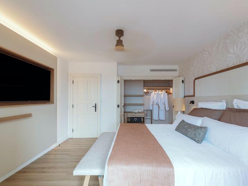 Modern hotel room with large bed, bench, and walk-in closet.