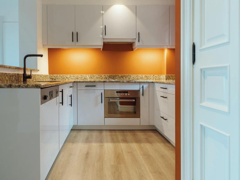 Modern kitchen with white cabinets, wooden countertop, and orange backsplash.