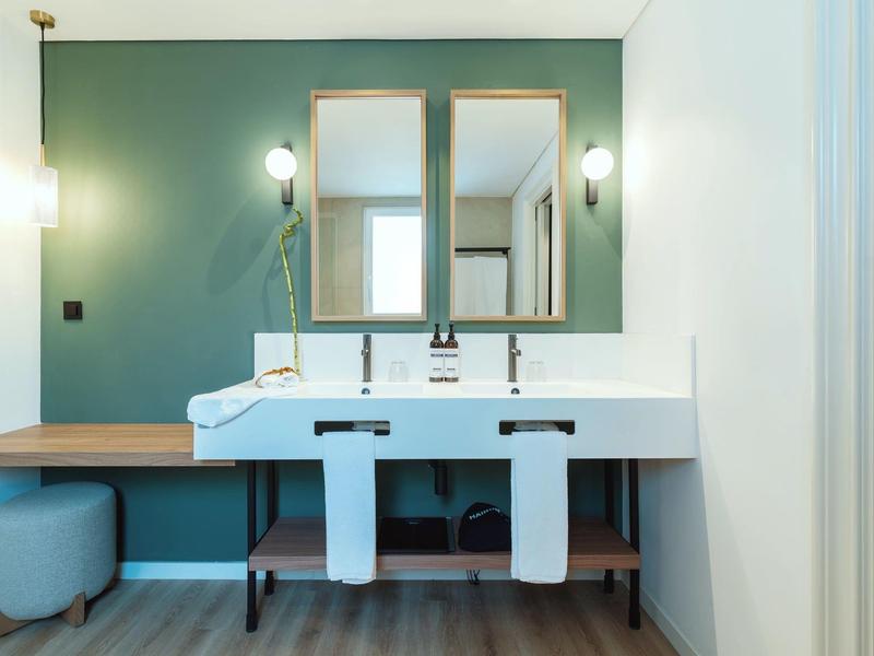 Modern bathroom with double sink, green wall, and two mirrors.