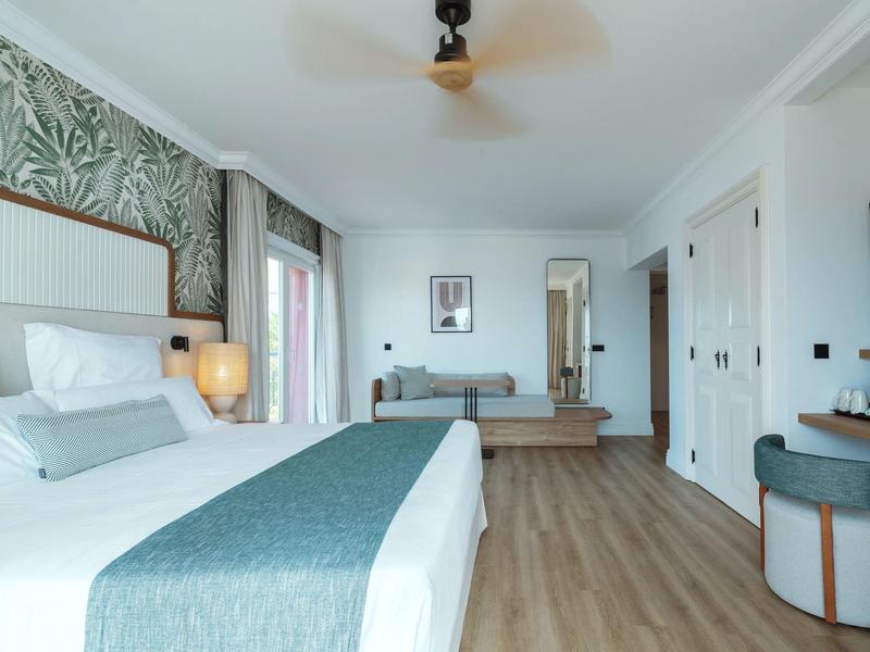 Bright hotel room with large bed, wooden floor, and decorative wall.