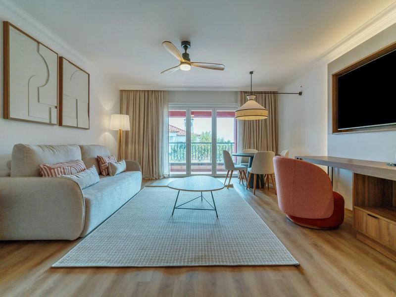 Bright living room with sofa, rug, table, red chair, and balcony view.